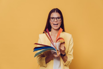 Young beautiful girl in yellow jacket over yellow background smiling and ho coloured paper and...