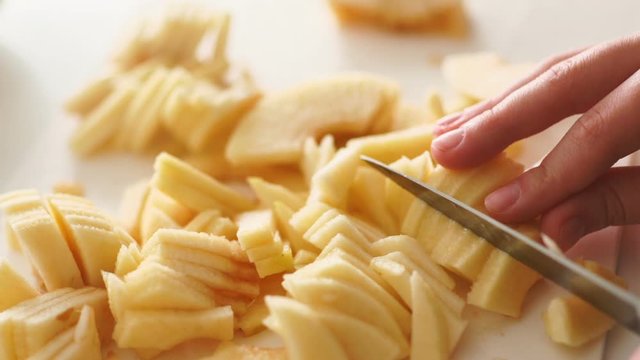 Close up of female hand cutting apple on slices. Preparing ingredients for baking apple pie. Chef slicing healthy apple at white plank in kitchen. Slicing peeled apples.