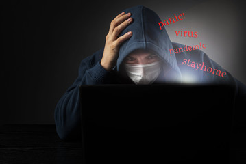 Words fly out of the laptop panic, pandemic, virus, stay home. Masked man reading pandemic news