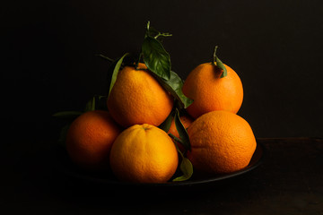 Naranjas frescas y naturales con hojassobre fondo oscuro. Vista de frente