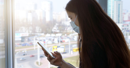 teenager girl in facemask with phone in hand window background