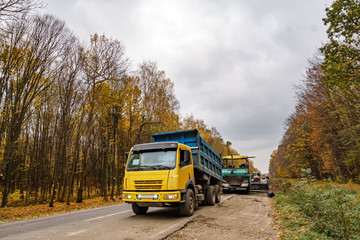 Fototapeta premium Road repair. Laying new asphalt. Heavy special machines. Truck in operation. Side view. Closeup.