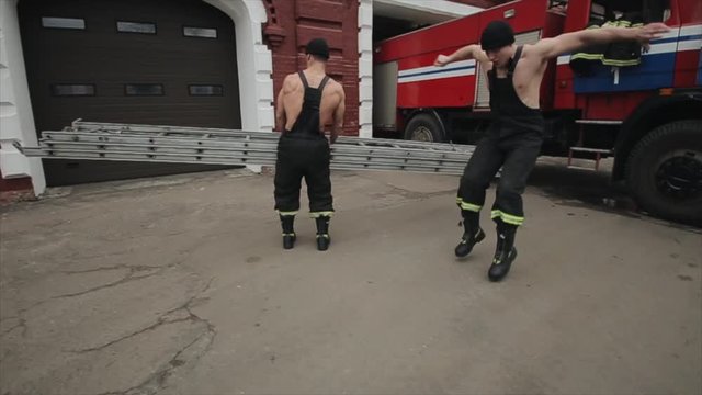 Two muscular young men are training near their fire engine. Jump and push-up