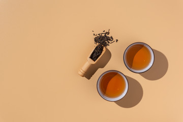 Two ceramic bowls with black puer tea ,dry pu-erh tea leaves in a wooden bamboo spoon on a beige background, tea ceremony,minimalism style.