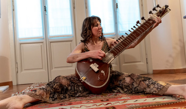 woman sitting on the floor is playing Indian sitar