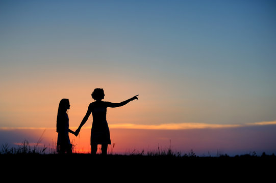 Silhouettes of mother and daughter against the sunset sky.
