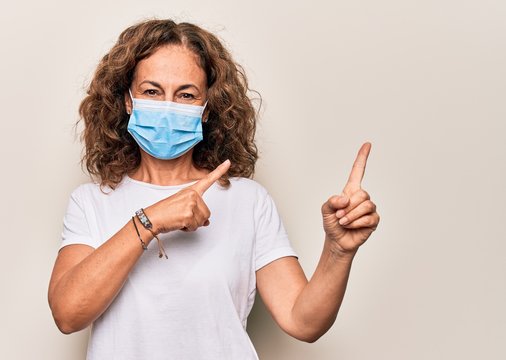 Middle Age Woman Wearing Coronavirus Protection Mask For Covid-19 Epidemic Virus Smiling And Looking At The Camera Pointing With Two Hands And Fingers To The Side.