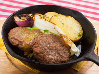 two steaks in a pan with potatoes eggs and onions