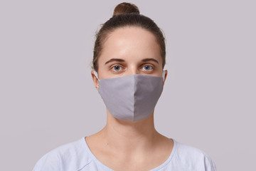 Closeup portrait of serious woman wearing gray protective mask, lady dresses white casual t shirt looking directly at camera, posing isolated over white background. Corona virus protection concept.