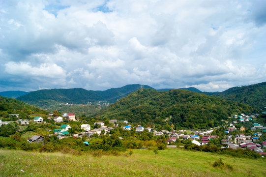 Horizontal photo - summer mountain landscape. Mountain villages, domius with colored roofs against the green and blue sky in white clouds