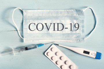 Medical mask, thermometer, pills, syringe on a blue wooden background. Text on the covid19 mask.
