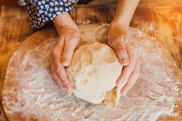 woman kneads the dough with her hands. female hands and raw dough on a wooden background. top view