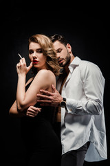 handsome man in white shirt touching confident, seductive woman with cigarette isolated on black