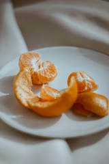 peeled tangerine with peel on a white plate on a fabric background close-up blurred background