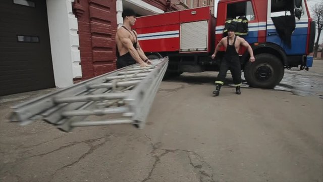 Men doing exercises and workout.A young muscular man twists a long metal staircase and another man jumps through it against the background of a fire truck. Close-up