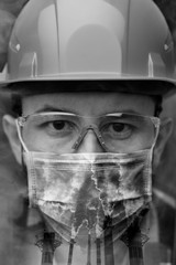Fototapeta premium Close-up portrait of a worker in a helmet, mask and goggles among smoke and exhaust pipes. Vertical orientation, double exposure.