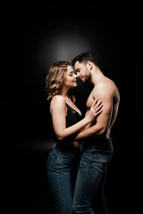 side view of sexy shirtless man and beautiful girl in bra hugging on black background