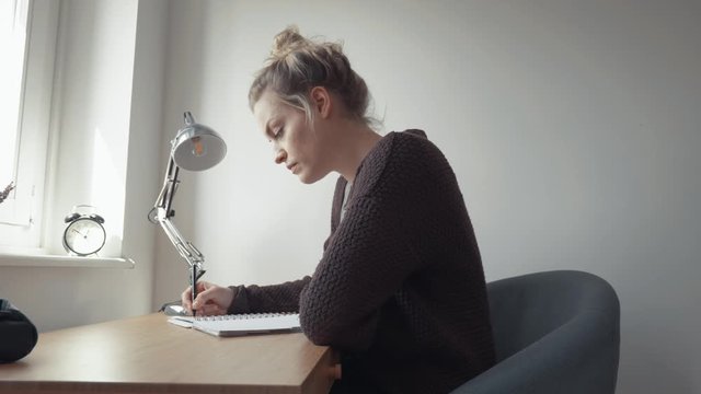 Young woman writes text alone at desk