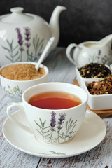 Detail of a mug with red tea with a teapot, brown cane sugar and dry tea leaves