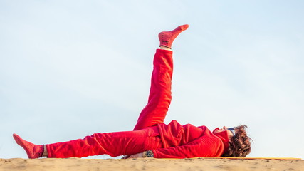 Beautiful mature woman doing gymnastics on a sandy beach on a background of autumn dawn.