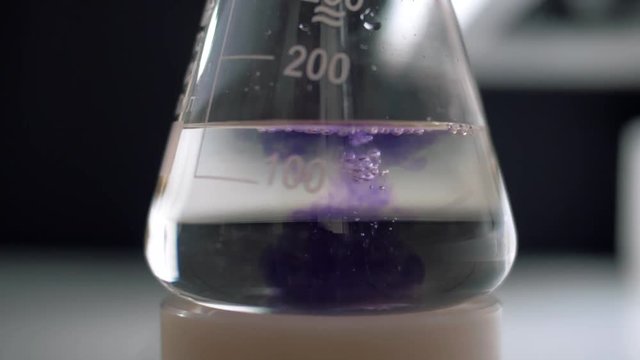 Laboratory assistant mixes reagents in a test tube flask for analysis. Slow motion