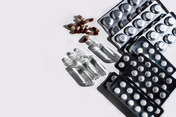 Medicines: white plain breakable tablets in transparent sticks, in metal non-trasparent sticks, overencapsulated tablets, ampuls with anti-virus vaccine on white background. Copy space.