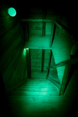 Mystical horror scary garret background to halloween. Old antique dirty wooden staircase in darkness in a mysterious paranormal spooky basement or attic with black shadow in the green light of a lamp