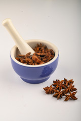 star anise in a blue ceramic spice mortar with a pestle on a white background. Close up.