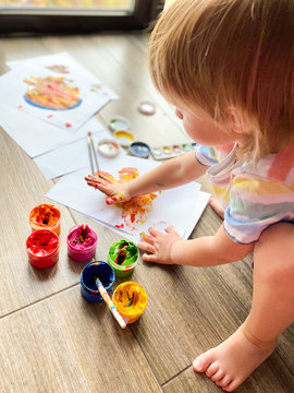
A fair-skinned little child / infant, draws with colorful paints against the background of a large panoramic window at home.