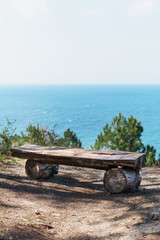 A single bench made of natural wood in the forest with a view of the sea.