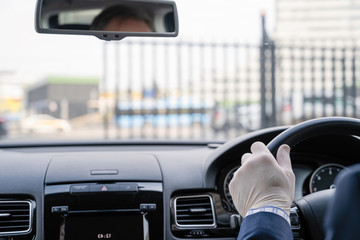 Middle age businessman in a blue suit and rubber gloves for protect himself from bacteria and virus driving a car. A male driver  in front of opening iron gate ready for a ride. Coronavirus. Pandemic.