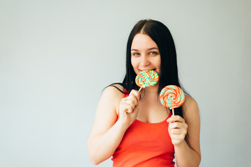 A cute cheerful girl in a bright orange t shirt is having fun and laughing with colorful lollipops in her hands - 339912987
