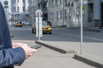 Businessman in a suit booking a taxi using mobile phone app standing on the street. yellow taxi car...