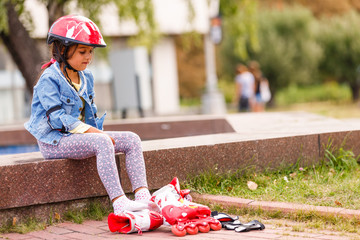 Three children sitting on a park bench after rollers
