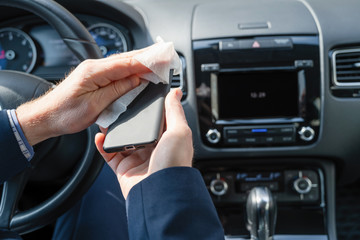 Middle age businessman in a blue suit cleaning mobile phone or gadget in a car using antivirus antibacterial wet wipe (napkin) for protect himself from bacteria and virus.