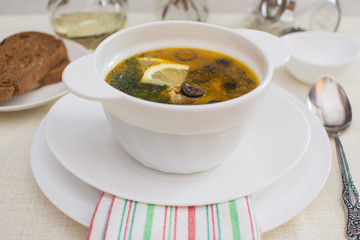Traditional Russian meat soup solyanka with sausages, lemon and olives in a white ceramic bowl.