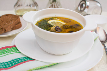 Traditional Russian meat soup solyanka with sausages, lemon and olives in a white ceramic bowl.