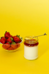 Red strawberry in glass jar and creamy white yogurt with jam on the yellow background