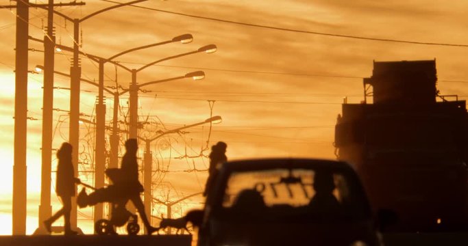 City life at sunset. Silhouettes. People with a pram and a dog cross the road on a pedestrian crossing, cars are passing by.