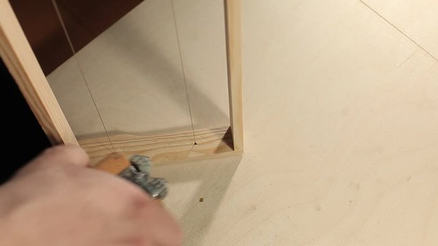 A man pulls strings or wire on a honey frame using a special device.