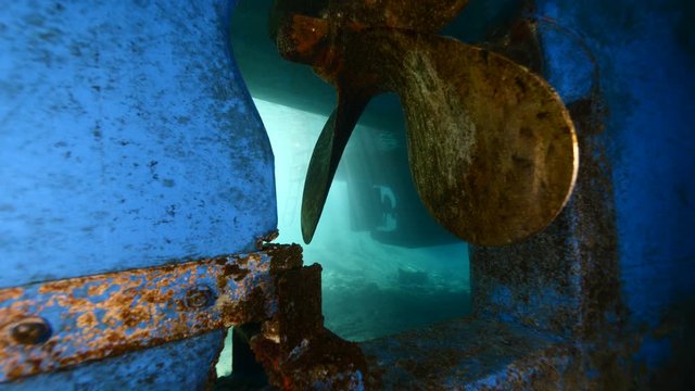 under boat scenery with scuba divers aroun the propeller of boat underwater