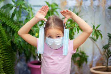 A little girl in a medical mask holds two more masks in her hands. Maximum protection during quarantine.