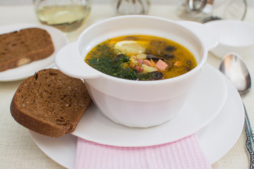 Traditional Russian meat soup solyanka with sausages, lemon and olives in a white ceramic bowl.