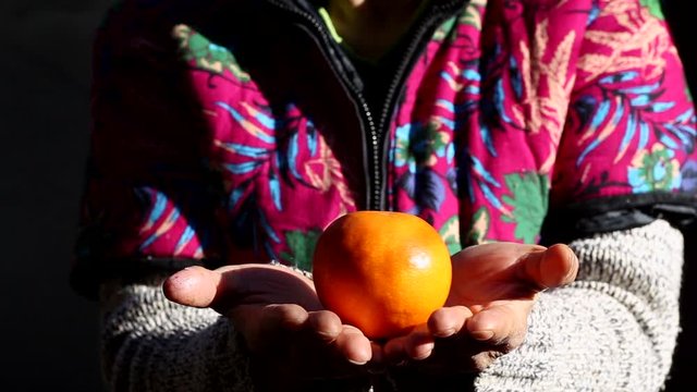 Middle-aged asian wonan dressed in traditional clothes holding orange in hand.