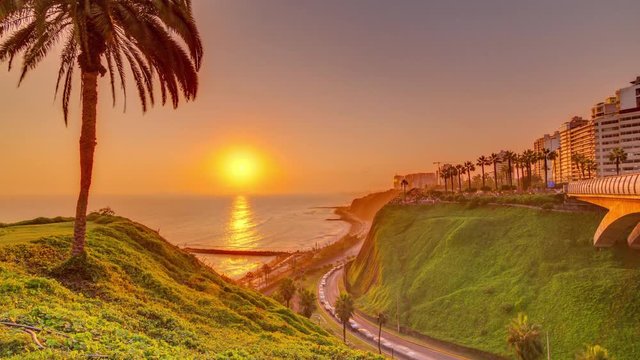 Aerial sunset view of Lima's Coastline in the neighborhood of Miraflores timelapse with orange light, Lima, Peru. Road with traffic and beach with ocean. Palm near Love park