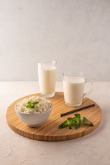 Milk in a cup, kefir in a glass and cottage cheese with herbs in a bowl on a wooden tray on a light background. Copy space