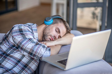 Young man in a checkered shirt sleeping on his laptop