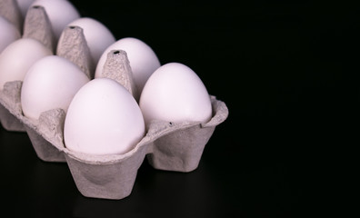 
Tray of white chicken eggs on a black background.Close-up. Copy space.