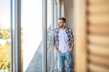 Young man in a checkered shirt looking out of the window
