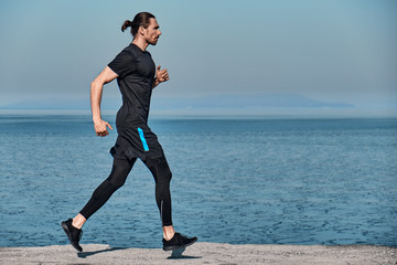 Side view of Healthy Handsome Active Man running on sidewalk in morning At Sea. Health conscious concept with copy space.